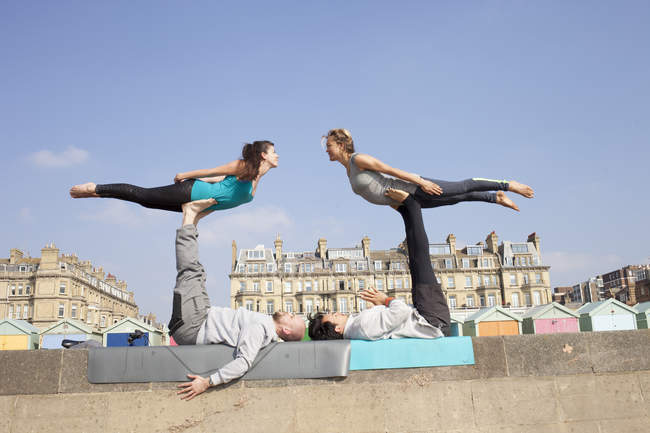 Hombres y mujeres practicando yoga acrobático en la pared de la playa de Brighton - foto de stock