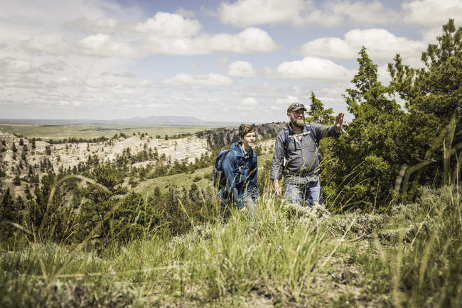 Padre señalando paisaje a hijo adolescente en viaje de senderismo, Cody, Wyoming, EE.UU. - foto de stock