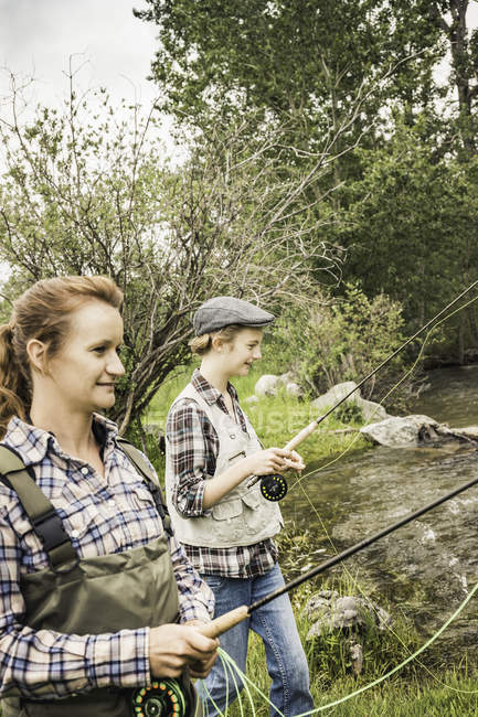 Side view of mother and daughter fishing in river smiling — Stock Photo