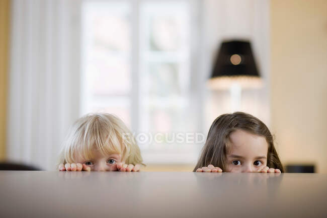 Дети смотрят через край стола — стоковое фото