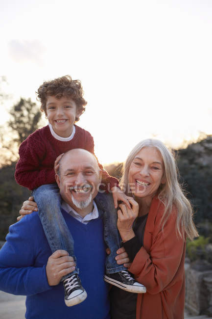 Großeltern mit Enkel auf den Schultern schauen lächelnd in die Kamera — Stockfoto