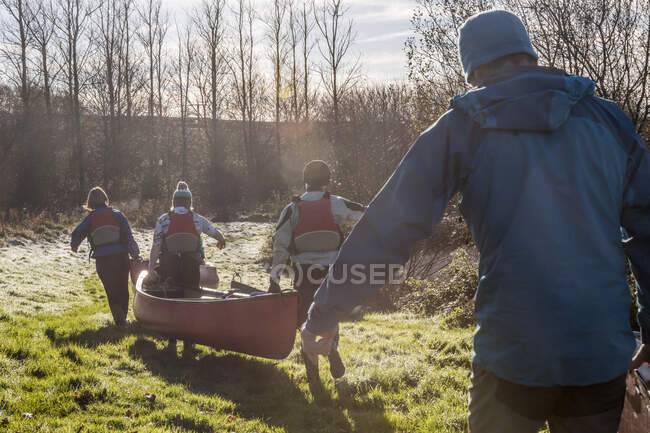 Four people carrying canoe across grass — Stock Photo