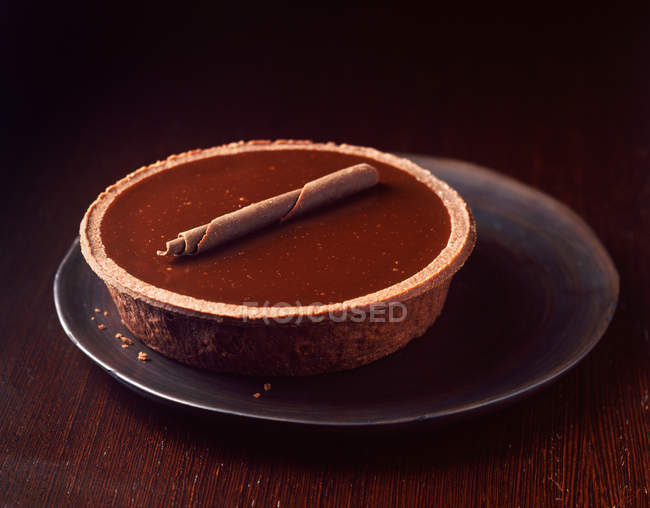 Whole chocolate tart with chocolate curl on plate — Stock Photo