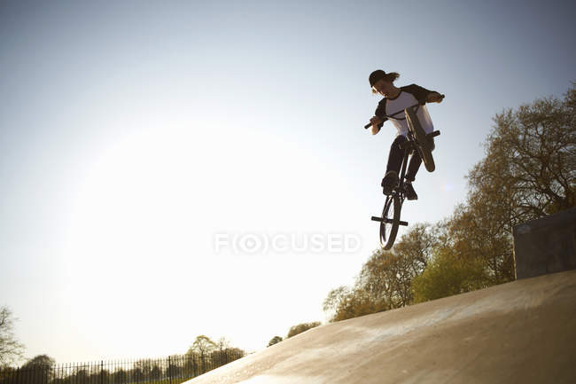 Joven, en el aire, haciendo acrobacias en bmx en skatepark - foto de stock