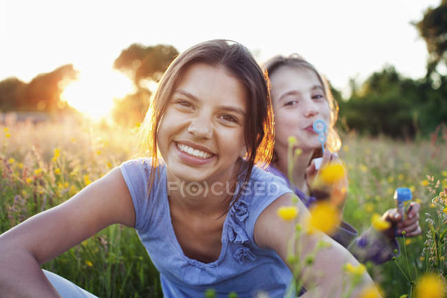 Portrait of girls sitting in field and one blowing bubbles — Stock Photo