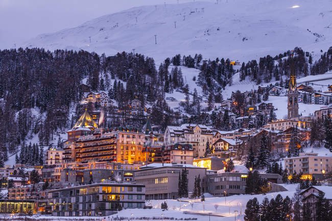 Dorf unter Bergen auf verschneiter Landschaft abends beleuchtet, sankt moritz, Schweiz — Stockfoto