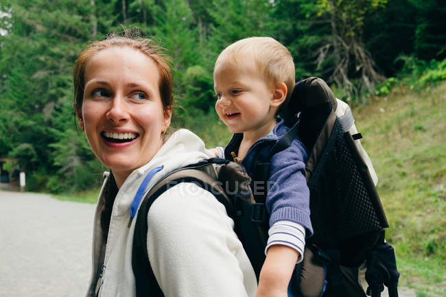 Junge Frau trägt Sohn auf dem Rücken nach draußen — Stockfoto