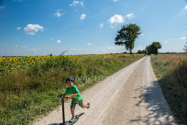 Niño corriendo por la carretera rural en scooter, Francia - foto de stock