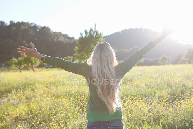 Rückansicht einer reifen Frau mit offenen Armen in einem Feld bei Sonnenuntergang — Stockfoto
