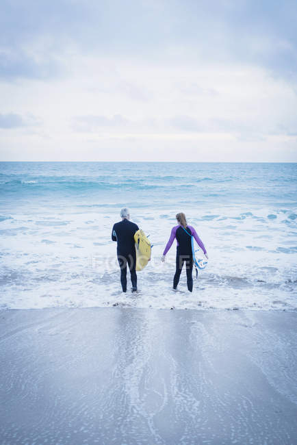 Rear view of male and female with surfboards in front of sea — Stock Photo