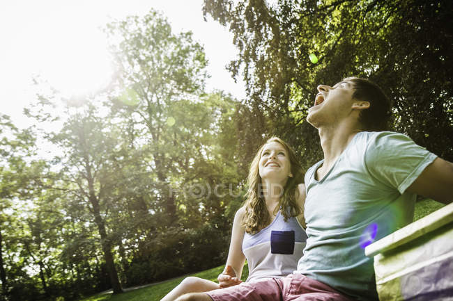 Young man trying to catch grape in his mouth, sitting with girlfriend in park — Stock Photo