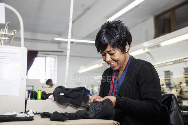 Женщина-работница фабрики снимает швы с черной ткани с запрограммированной вышивальной машины на швейной фабрике — стоковое фото