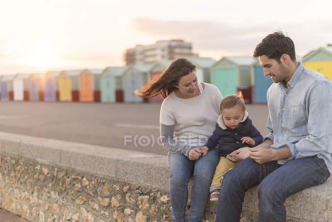Junge Familie sitzt auf Strandmauer — Stockfoto
