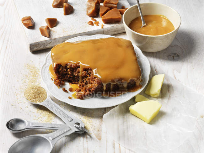 Sticky toffee pudding on white plate and hot toffee sauce in bowl — Stock Photo