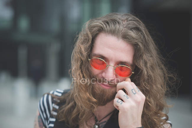 Portrait de jeune hippie mâle avec lunettes de soleil orange et doigts tatoués — Photo de stock