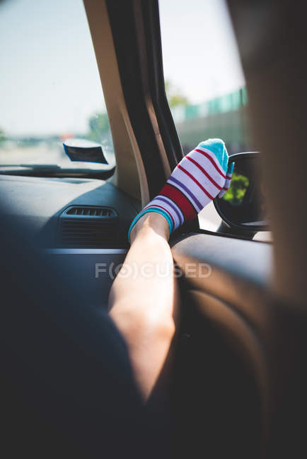 Jambe avec des chaussettes rayées colorées sur la fenêtre de la voiture — Photo de stock