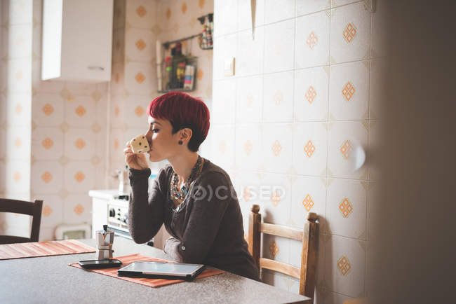 Молода жінка сидить за столом п'є каву — стокове фото