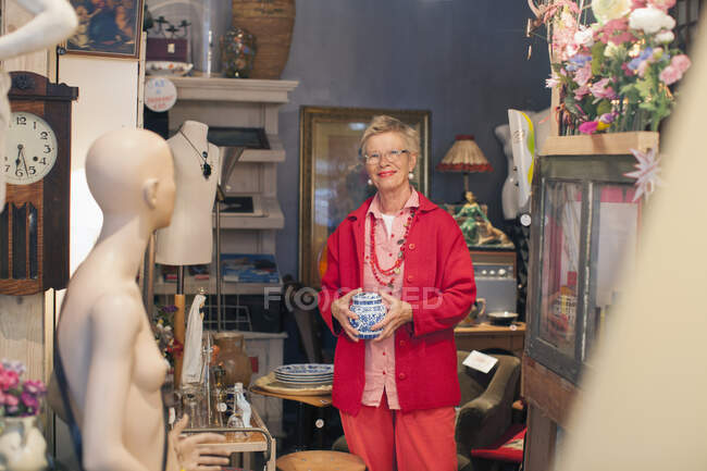Portrait of mature woman holding china pot in vintage shop — Stock Photo
