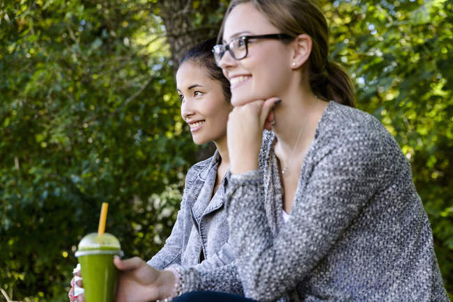 Две молодые женщины с кофе на вынос сидят в парке — стоковое фото