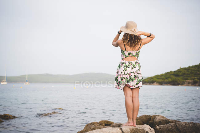 Mulher olhando para o mar, usando chapéu, visão traseira — Fotografia de Stock