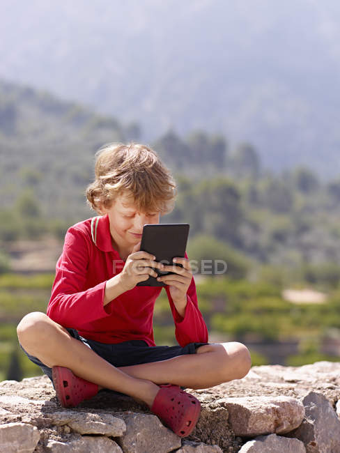 Хлопчик сидить на кам'яну стіну дивлячись на цифровий планшет, Майорка, Іспанія — стокове фото