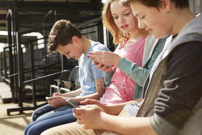 Quatro meninos e meninas lendo textos de smartphones no stand do estádio — Fotografia de Stock