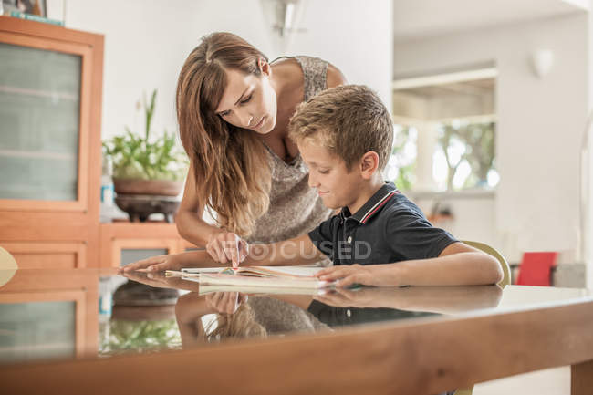 Mother and son looking down at homework at dining room table — Stock Photo