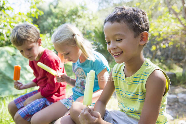 Tres niños comiendo helados en el jardín - foto de stock