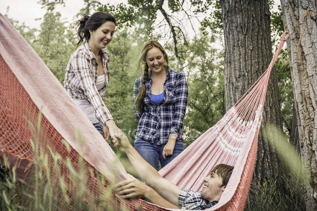 Two young women helping young man from hammock — Stock Photo