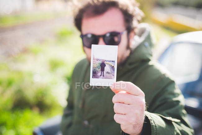 Portrait of mid adult man holding up an instant photograph of himself — Stock Photo
