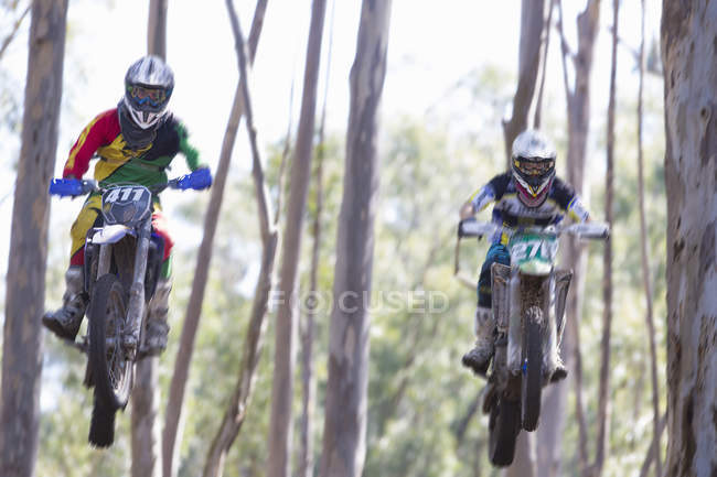 Dois jovens pilotos de motocross do sexo masculino pulando no ar através da floresta — Fotografia de Stock