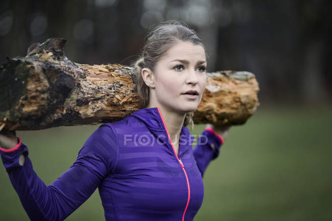 Jovem mulher carregando ramo de árvore no ombro olhando para longe — Fotografia de Stock