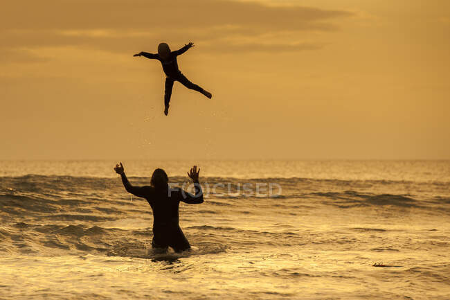 Père jetant son fils dans l'air, dans la mer au coucher du soleil, Lahinch, Clare, Irlande — Photo de stock