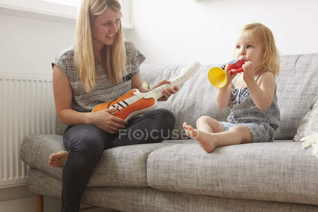 Малюк і мати грають з іграшковою трубою і гітарою на дивані — стокове фото