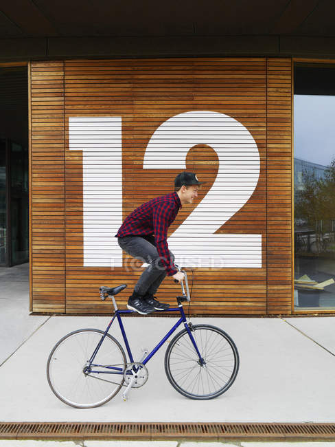 Urbane Radfahrer balancieren auf Fahrrad vor nummerierten Holzwand — Stockfoto