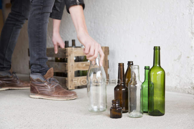 Teenage boy placing empty bottles into wooden crate in garage — Stock Photo