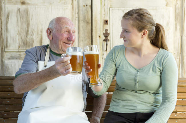 Senior und junge Frau stoßen mit Bier an — Stockfoto