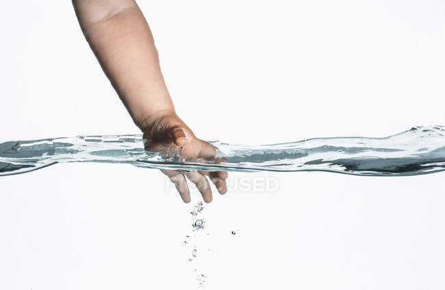 Vista a nivel de superficie de la mano de los niños pequeños que llegan al agua clara - foto de stock