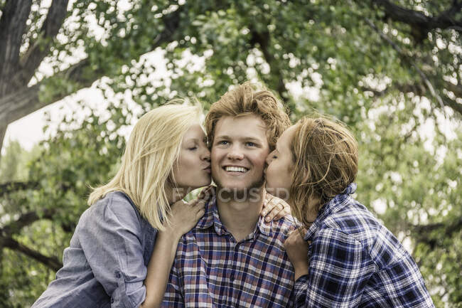 Adolescente et jeune femme embrassant jeune homme heureux sur la joue — Photo de stock