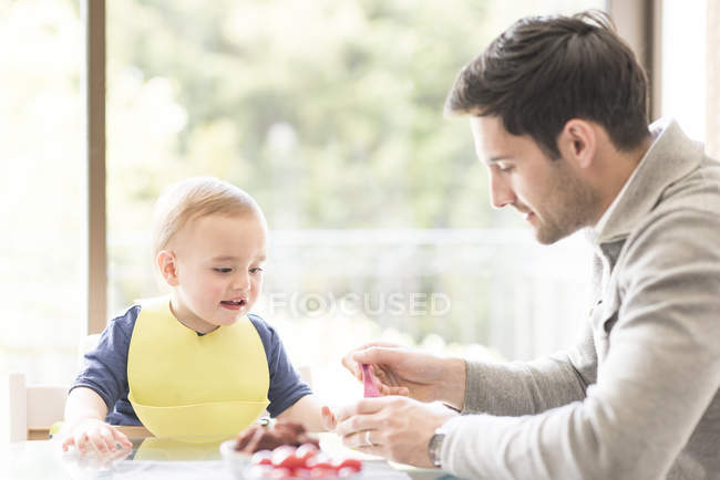 Батько годує молодого сина, в приміщенні — стокове фото