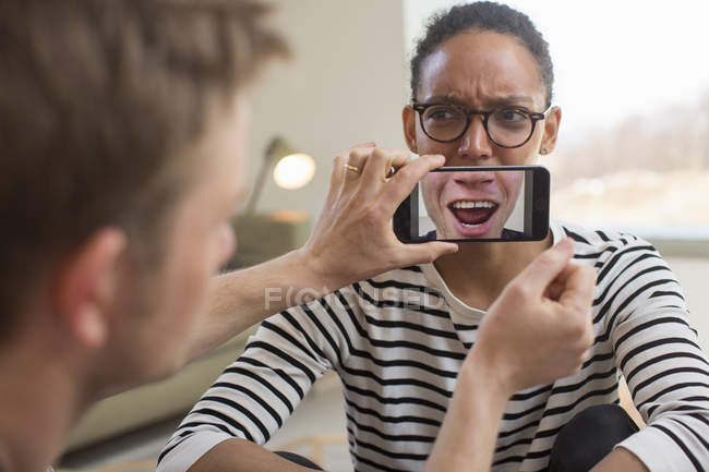 Man holding smartphone in front of woman mouth — Stock Photo