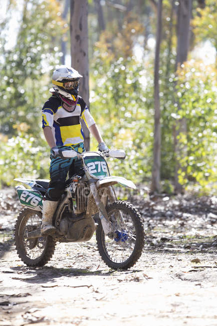 Young male motocross racer standing whilst riding through forest — Stock Photo
