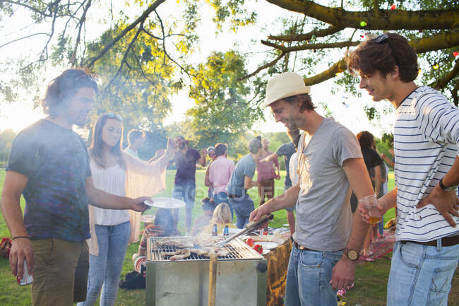 Happy adult friends barbecuing at sunset party in park — Stock Photo