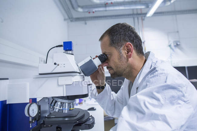 Asistente de laboratorio masculino mirando en el gadget del microscopio - foto de stock
