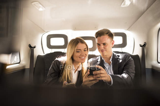 Businessman and businesswoman using smartphone in black cab, London, UK — Stock Photo