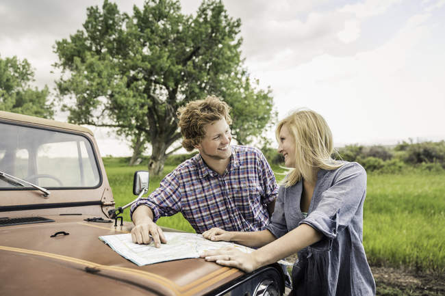 Teenage girl and boyfriend reading map on jeep hood — Stock Photo