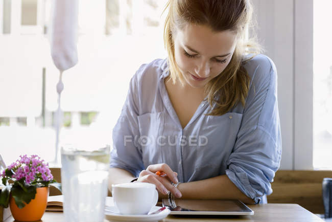 Молода жінка в кафе пише, дивлячись на камеру посміхається — стокове фото