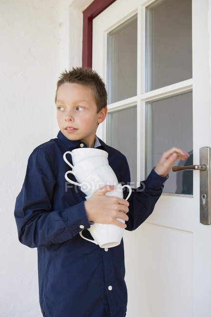 Boy carrying stack of cups on patio — Stock Photo