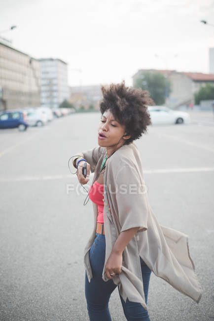 Young woman walking and dancing to earphone music in city carpark — Stock Photo