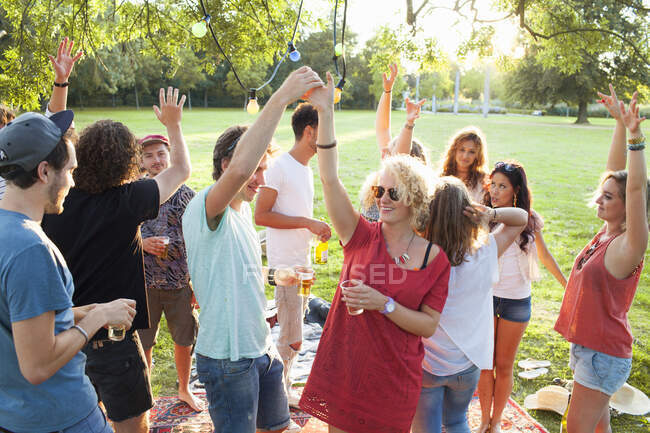 Multitud de amigos adultos bailando en la fiesta en el parque al atardecer - foto de stock